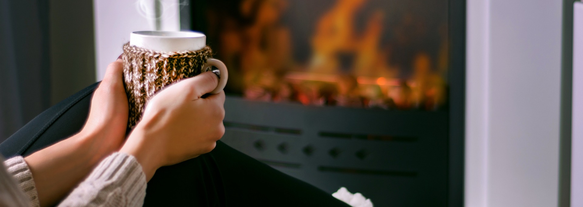 woman sitting in front of fireplace with hot beverage